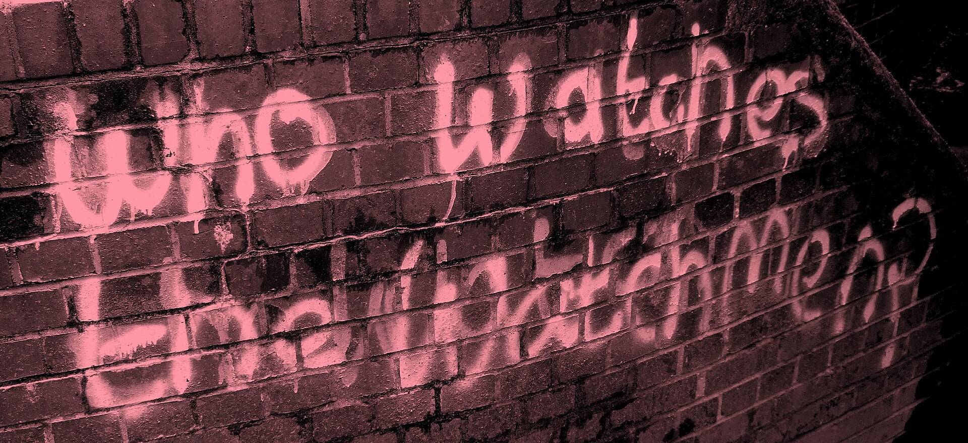 Graffiti on a brick wall: “Who watches the watchmen?”
